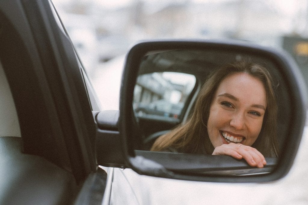 happy used car buyer looks in side mirror