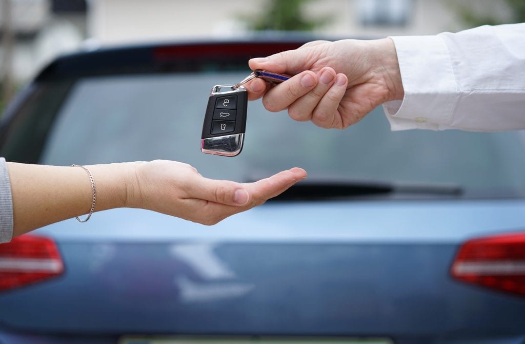 salesperson hands key to car buyer